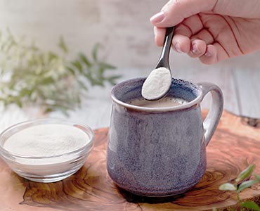 Femme qui verse de la poudre de collagène dans une tasse de café