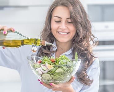 Jeune femme qui met de l'huile dans sa salade méditerrannéenne