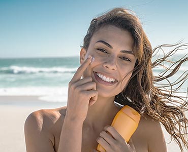 Jeune femme à la plage qui se met de la crème solaire sur le visage