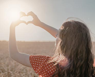 Jeune femme au soleil qui fait un coeur avec les mains