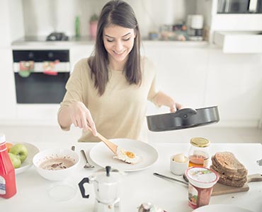 Jeune femme cuisinant un oeuf au plat