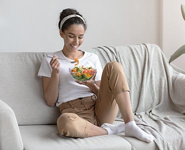 Jeune femme qui dine sur le canapé